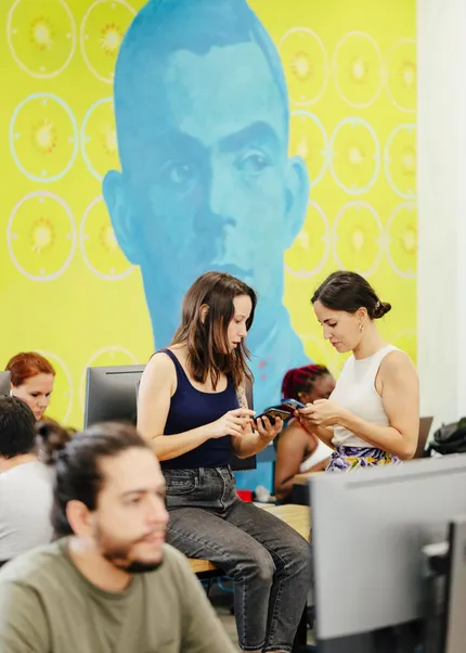 The Head of Marketing at Z1 is reviewing the UI of a project in Figma on her phone with a colleague.